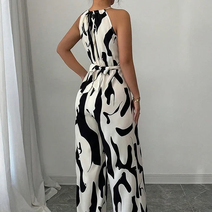 Back view of black and white backless jumpsuit with abstract print, worn by a model in a simple indoor setting.