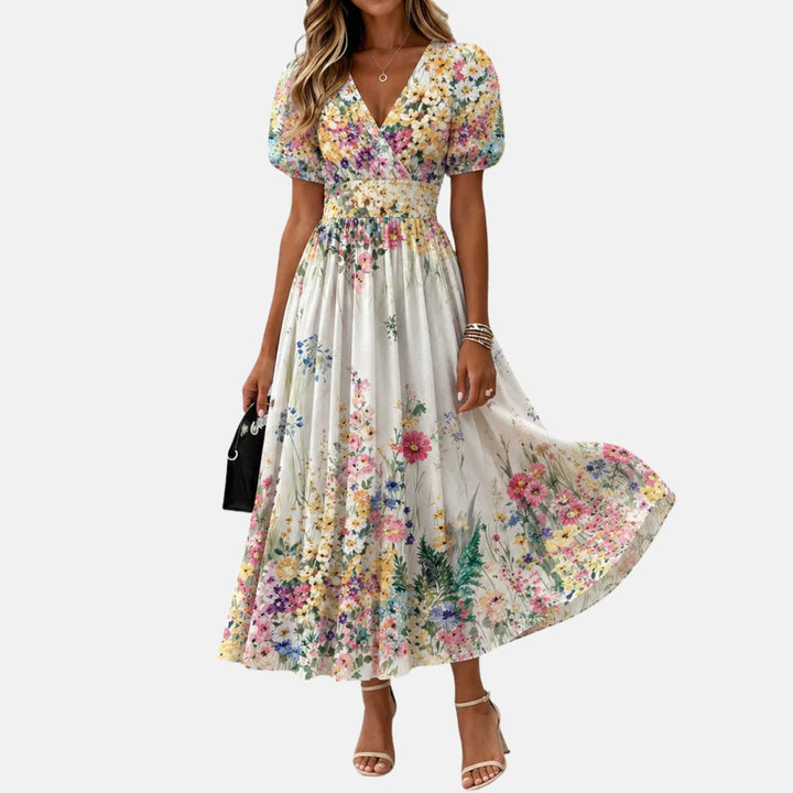 Floral midi dress with puff sleeves and V-neck, displayed in a studio. Model carries a small black handbag.