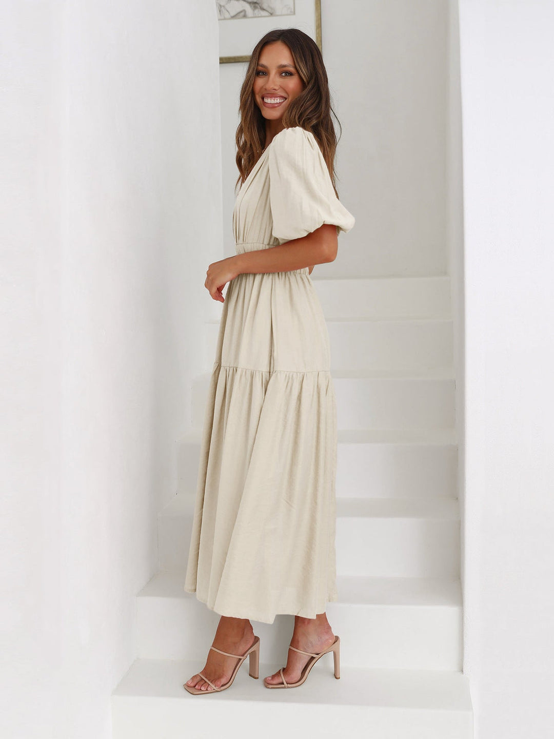 Woman in a cream midi dress with puff sleeves, standing sideways on white stairs.