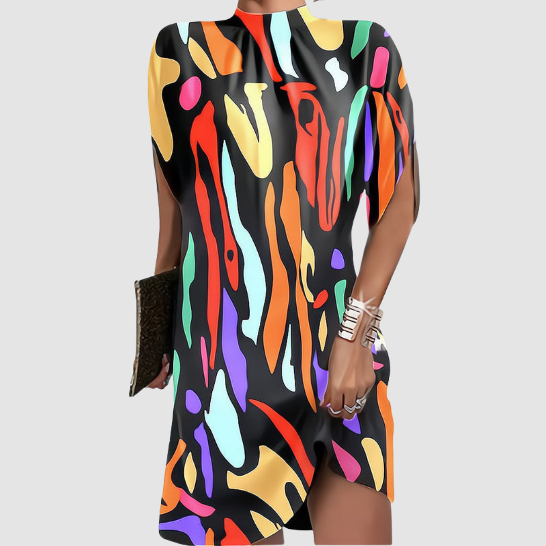 Colorful abstract patterned knee-length dress with loose fit, high neckline, paired with gold bangles and clutch against gray.