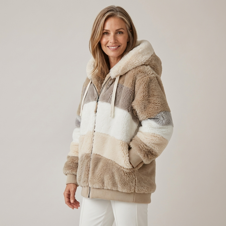 Woman wearing a plush, multicolored hooded jacket in white, brown, and beige stripes, in a studio setting.