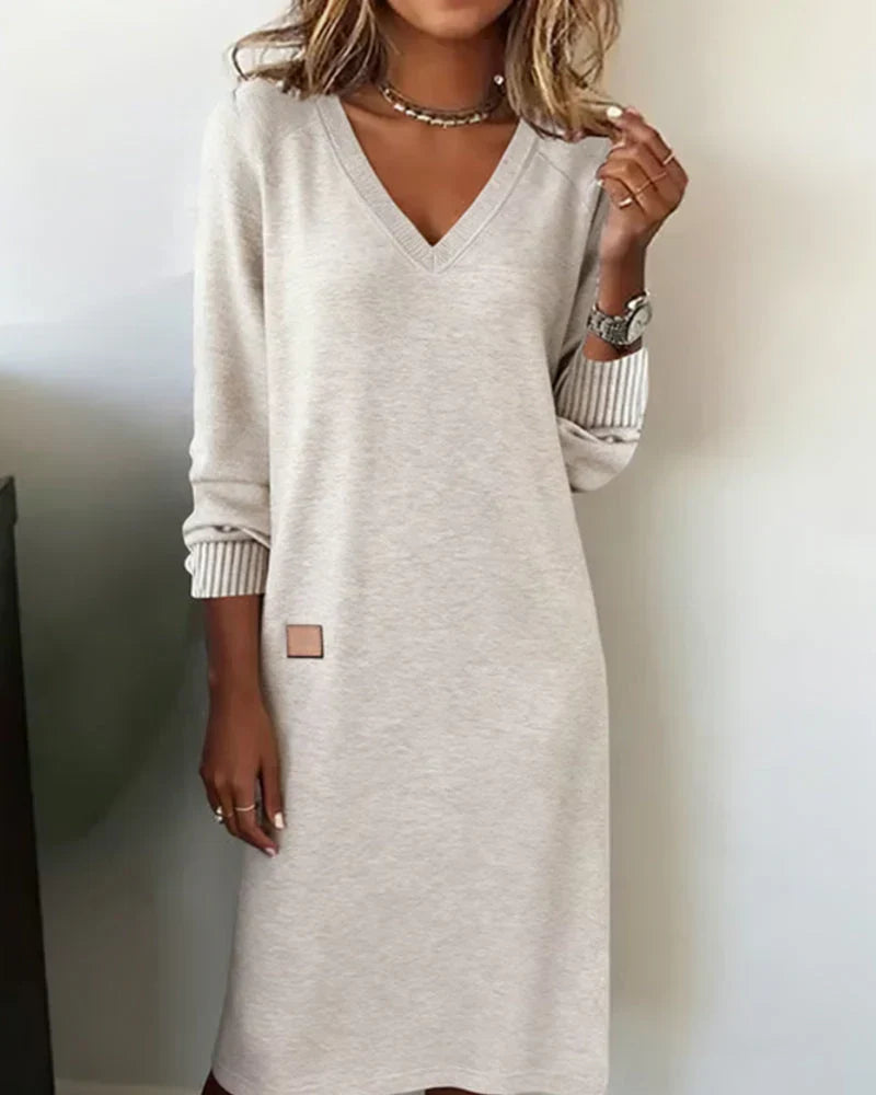 Light grey cozy dress with V-neck and long sleeves, worn indoors.
