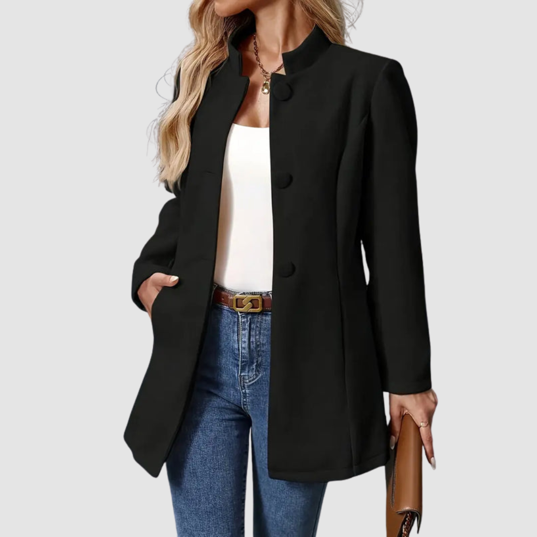 Black jacket, large buttons, worn over white top and jeans, holding clutch, plain background.