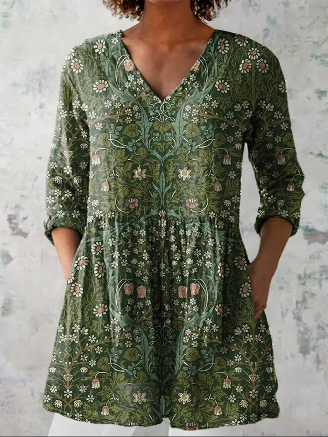 Green vintage floral V-neck dress with long sleeves, worn by model with hands in pockets against a textured wall backdrop.