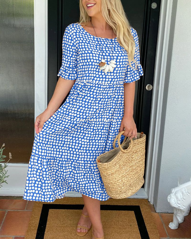 Woman in blue and white polka dot summer dress, holding a straw tote, standing by a door.