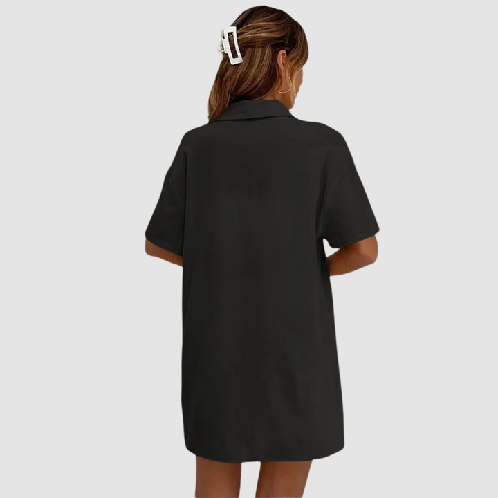 Back view of woman in black button-up dress, hair clipped, against a studio background.
