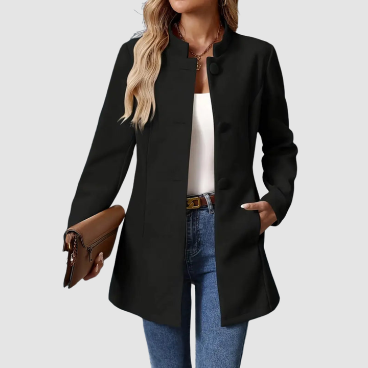Black jacket, large buttons, worn over white top and jeans, holding clutch, plain background.
