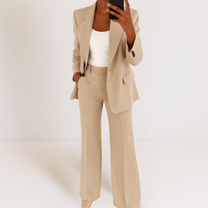 Beige two-part suit set with tailored fit, white top, hands in pockets, studio background.