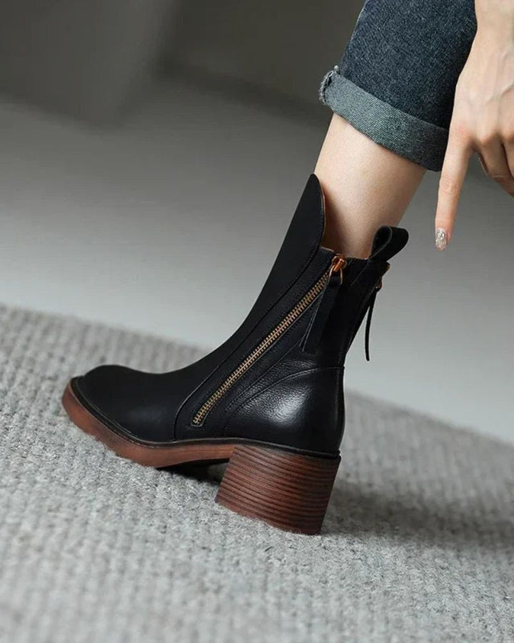 Close-up of black leather boots with zippers, worn with rolled jeans on a textured carpet indoors.