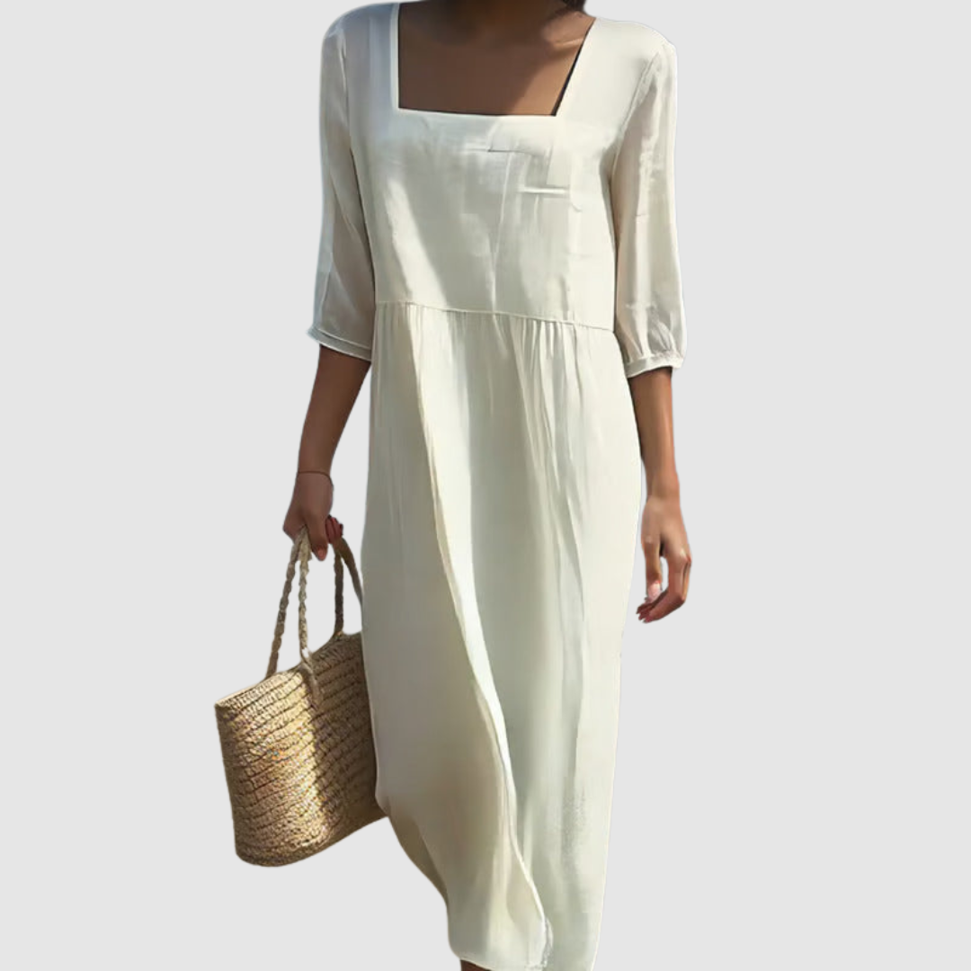 Woman in an off-white, flowing casual dress with three-quarter sleeves holding a woven bag against a plain studio background.