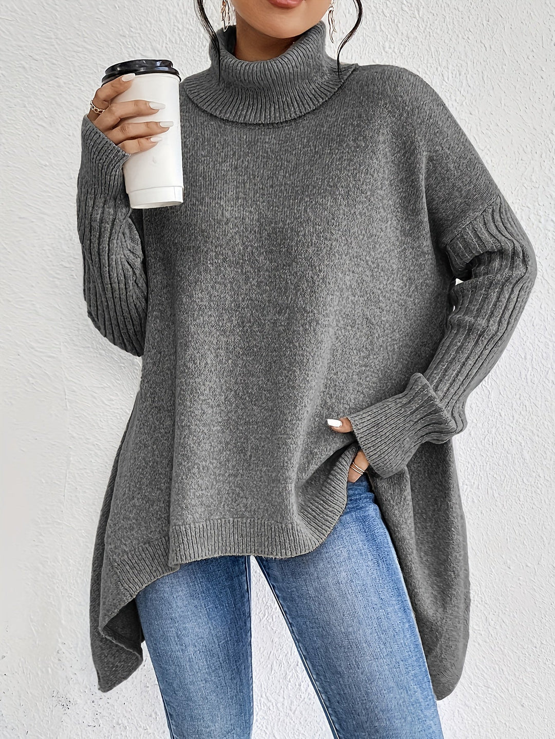 Gray turtleneck sweater with ribbed sleeves, holding a coffee cup, paired with jeans against a white background.