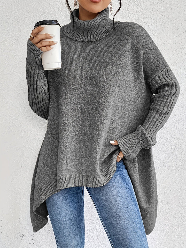 Gray turtleneck sweater with ribbed sleeves, holding a coffee cup, paired with jeans against a white background.