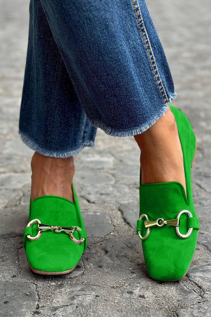 Bright green loafers with metal detail, worn with frayed jeans on cobblestone street.