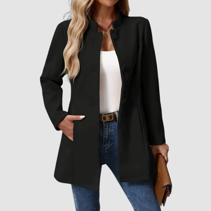 Black jacket with large buttons, worn over white top and jeans, holding a clutch, plain background.