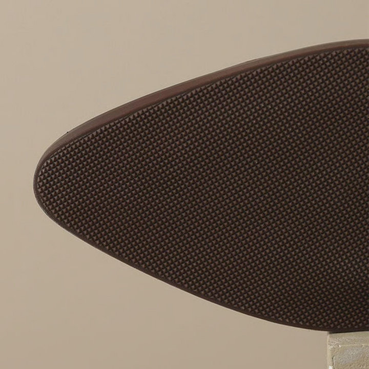 Close-up of brown ankle boot sole, showcasing textured grip on a neutral background.