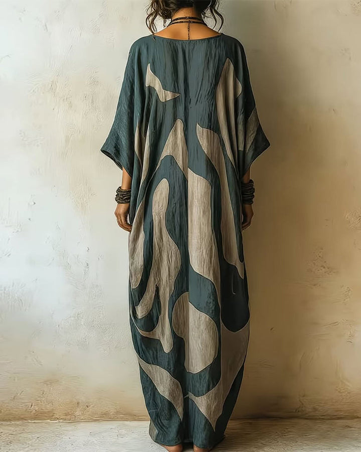 Back view of maxi dress with striking abstract patterns, complemented by rustic accessories, in a textured indoor environment.