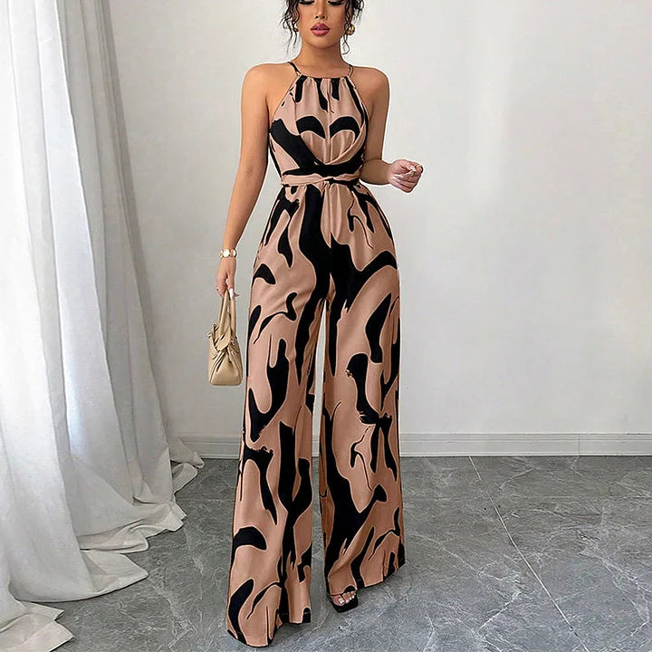 Brown and black patterned backless jumpsuit on a model, posed indoors with white drapery and natural light.