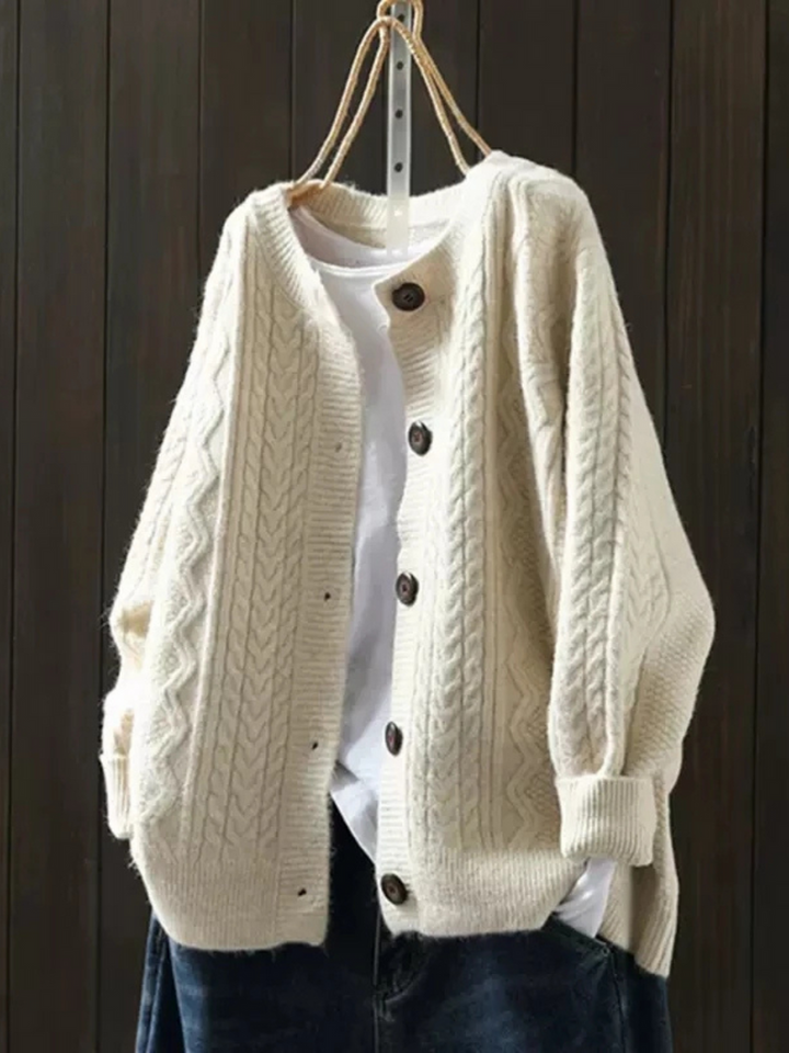 Cream knitted cardigan with button closure, layered over a white shirt, hanging against a dark wood background.