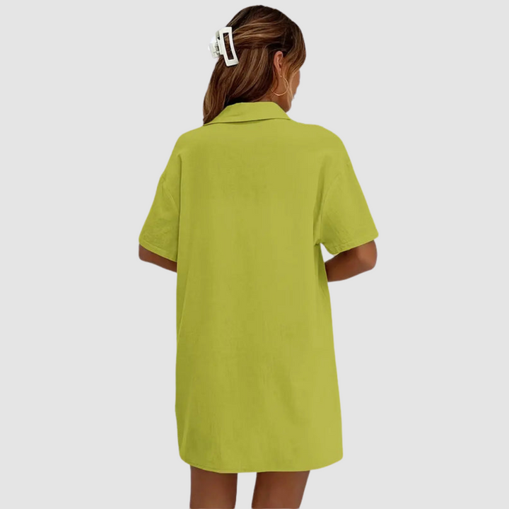 Back view of woman in green button-up dress, hair clipped, against a studio background.