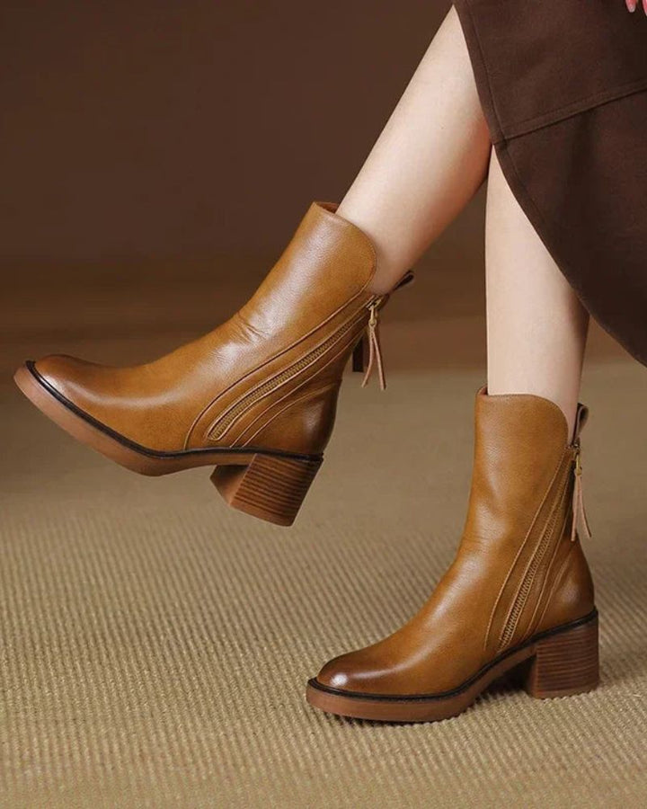 Tan ankle boots with side zippers worn with brown dress on tan carpet.