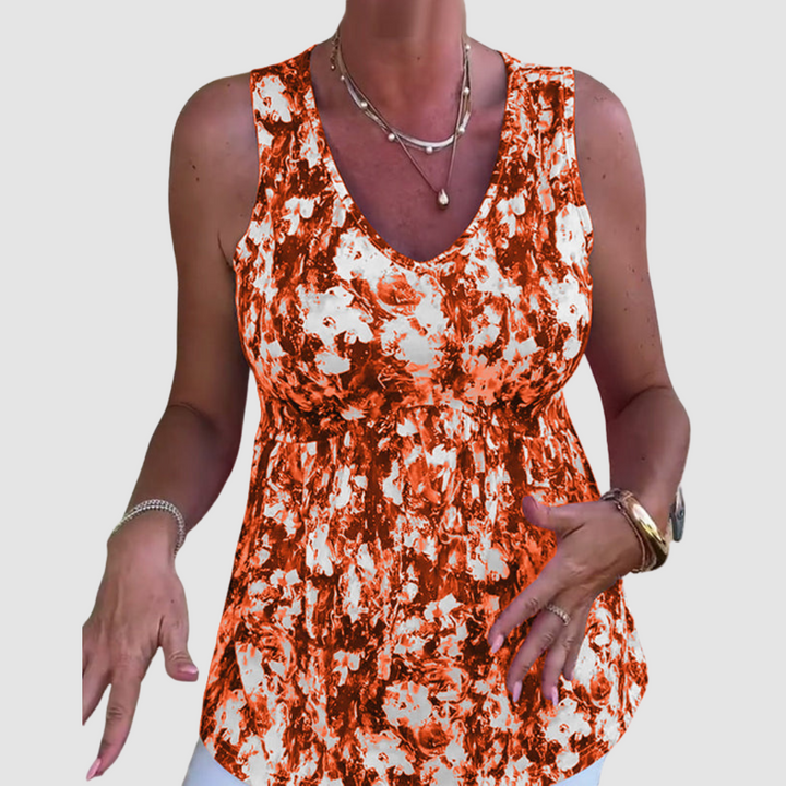 Woman in orange and white patterned sleeveless top, gesturing with hands, in a studio setting.