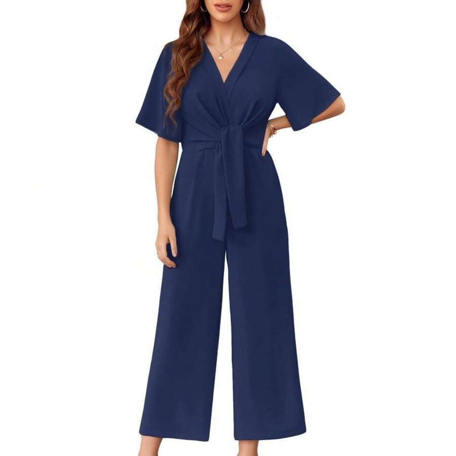 Blue elegant jumpsuit with short sleeves and a tie waist on a woman, studio background.
