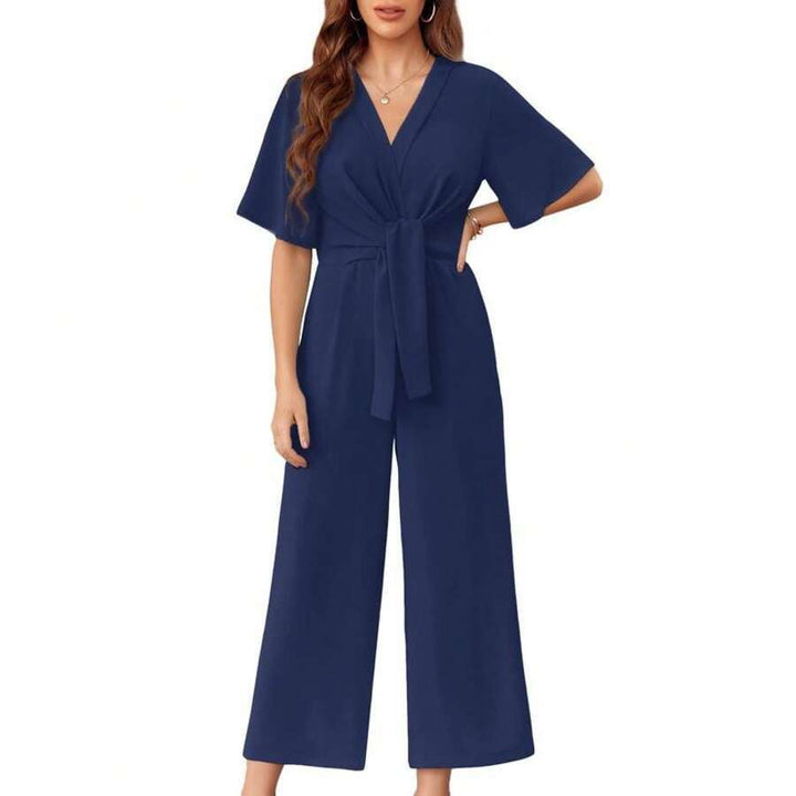 Blue elegant jumpsuit with short sleeves and a tie waist on a woman, studio background.