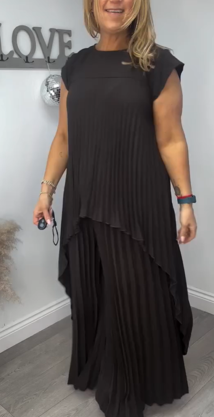 Woman modeling a black pleated midi top and wide-leg pants set in a cozy room with decor on the wall.