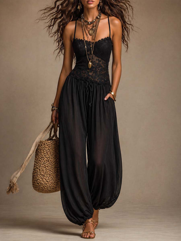 Elegant black jumpsuit with lace top and flowy pants, accessorized with layered jewelry and a woven bag in a studio setting.