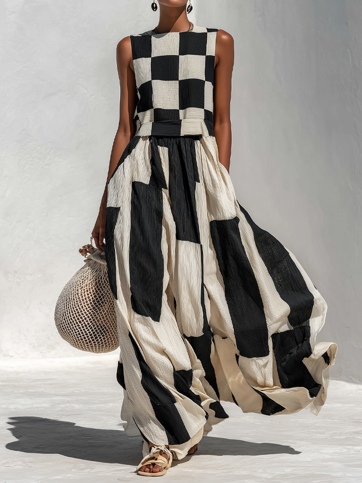 Model wearing a black and white contrast panel sleeveless maxi dress, holding a crochet bag, standing on a light textured studio floor.