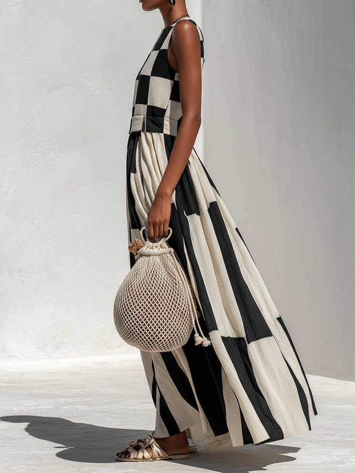 Side profile of a model wearing a black and white contrast panel maxi dress with a crochet bag, standing on a light floor.