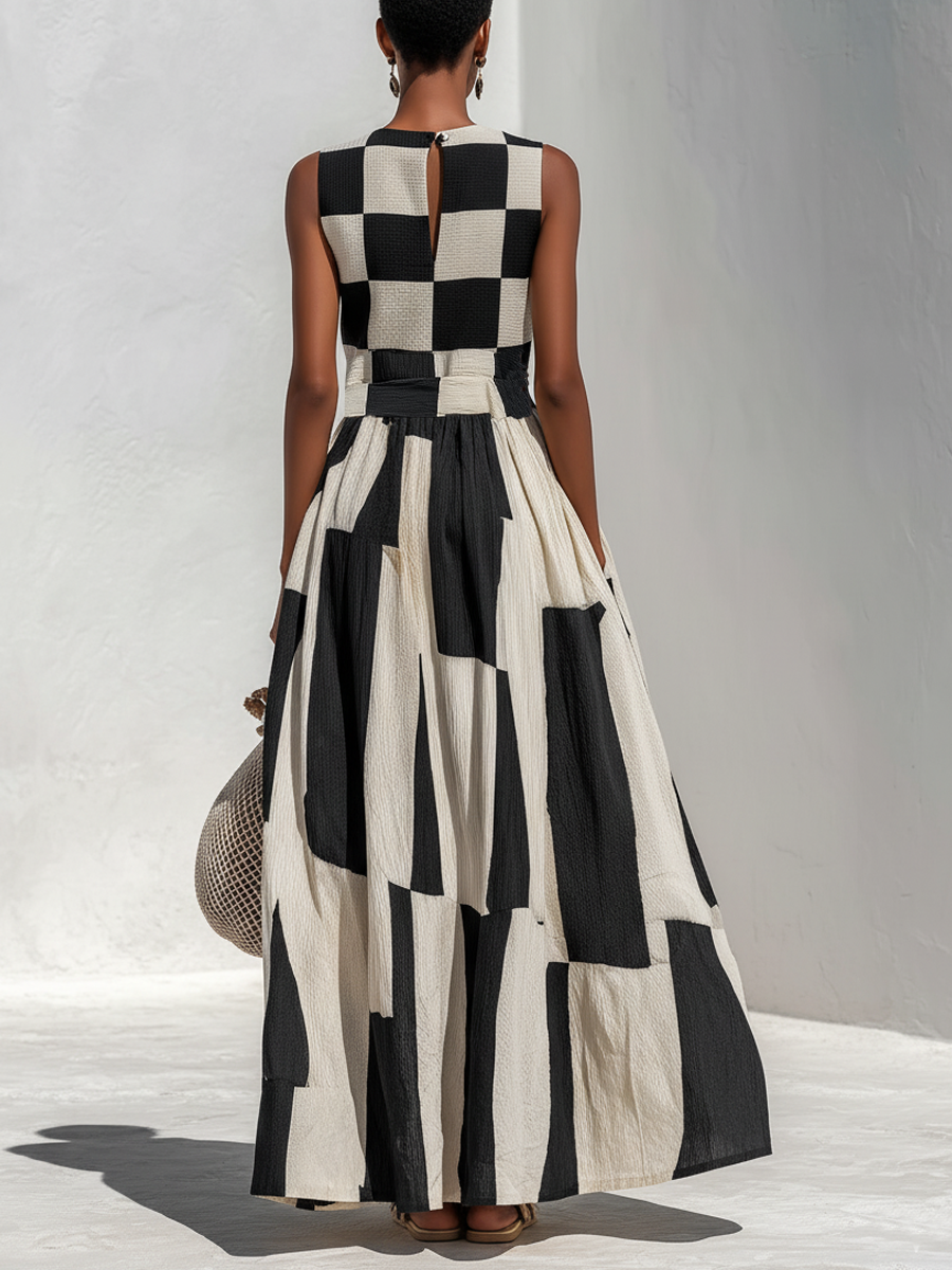 Back view of a model in a black and white checkered sleeveless maxi dress, holding a crochet bag, on a light textured floor.