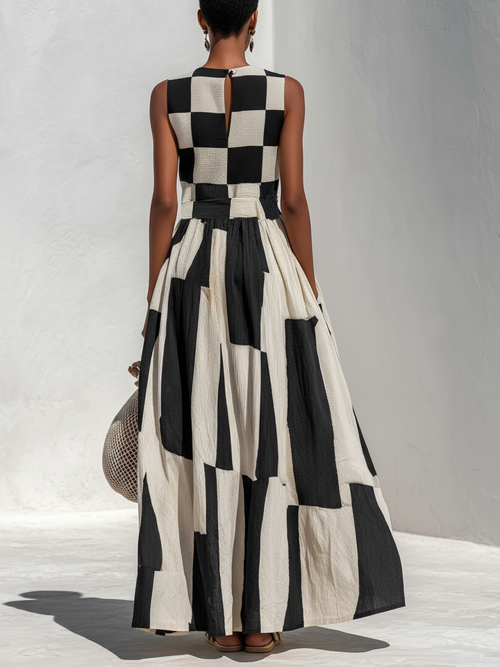 Back view of a model in a black and white checkered sleeveless maxi dress, holding a crochet bag, on a light textured floor.