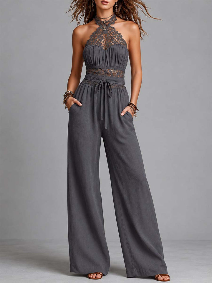 Gray halterneck jumpsuit with lace detailing, wide legs, and a tie waist, modeled in a studio setting.