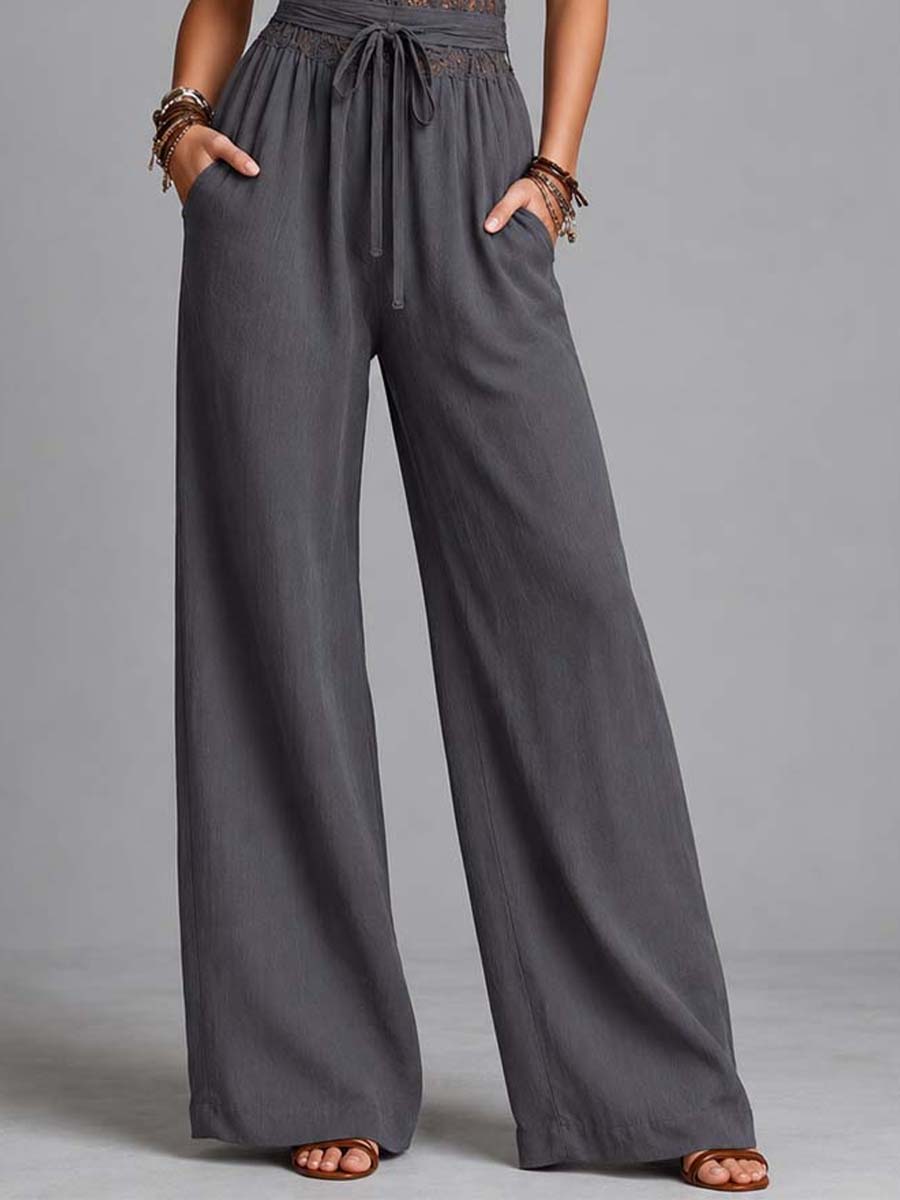 Close-up of wide-leg pants with tie waist on a gray jumpsuit, modeled in a studio.