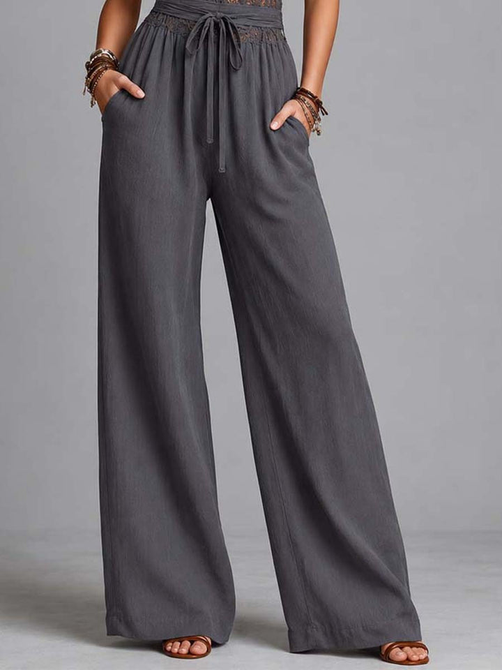 Close-up of wide-leg pants with tie waist on a gray jumpsuit, modeled in a studio.