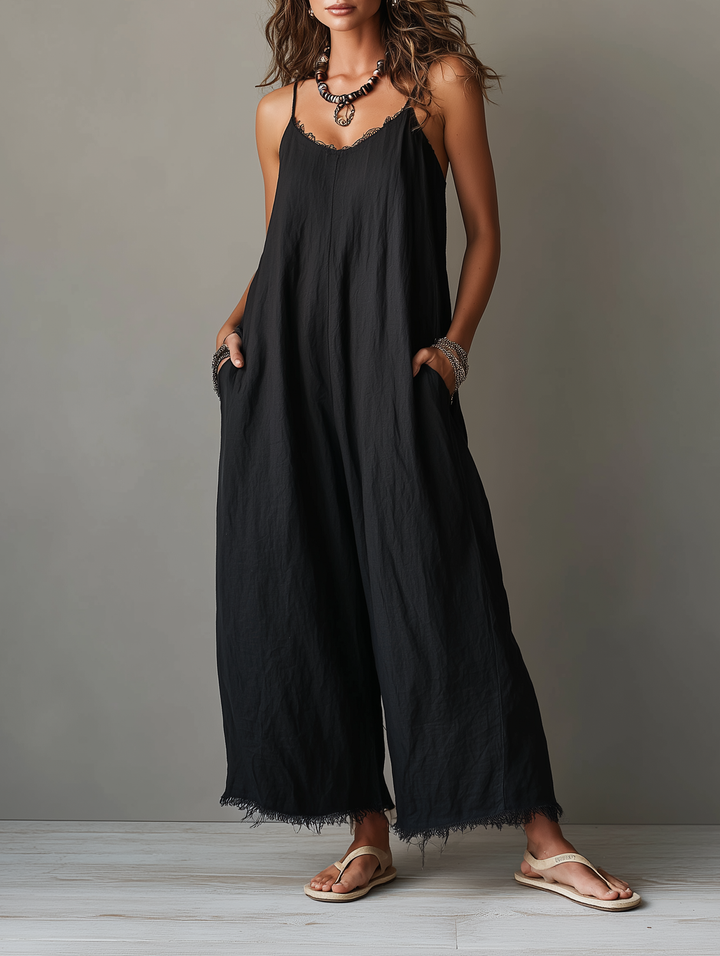 Black jumpsuit with spaghetti straps and fringed hem, worn by a model in sandals in a studio setting.