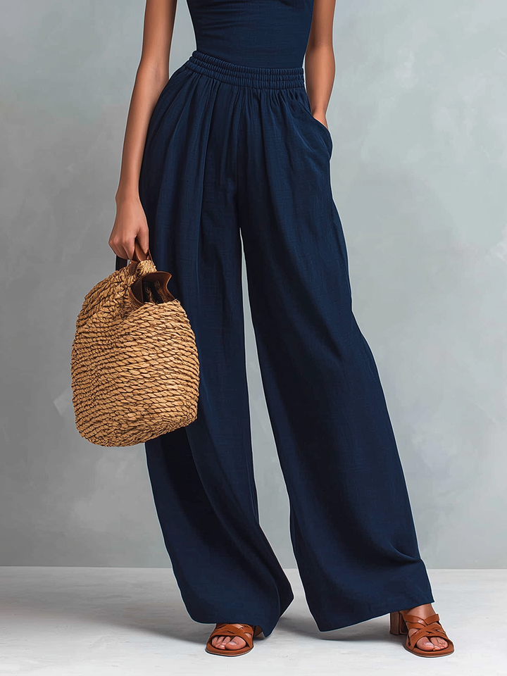 Focus on the lower half of a dark blue jumpsuit with wide legs and sandals, holding a woven bag.