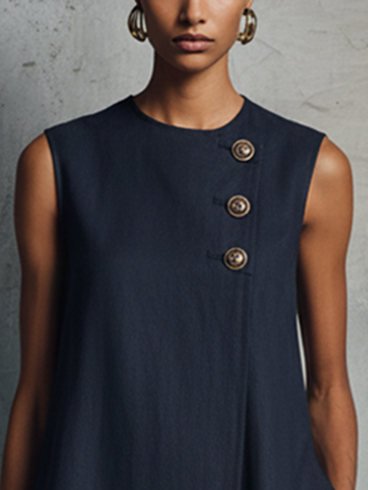 Close-up of navy dress upper section with three decorative buttons, worn by model, in industrial setting.