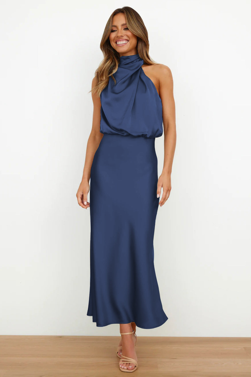 Navy blue sleeveless halter dress with a graceful silhouette in a minimal indoor setting.