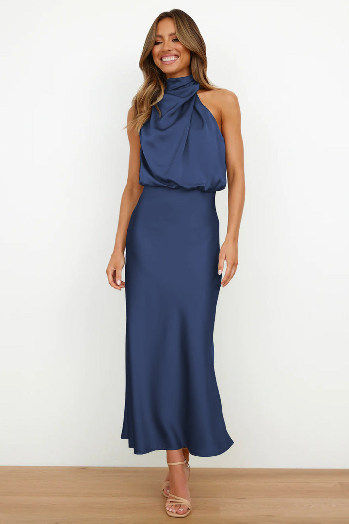 Navy blue sleeveless halter dress with a graceful silhouette in a minimal indoor setting.