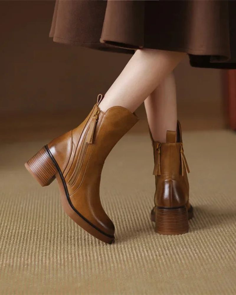 Back view of brown leather boots with zippers, styled with a dress on a beige carpet indoors.