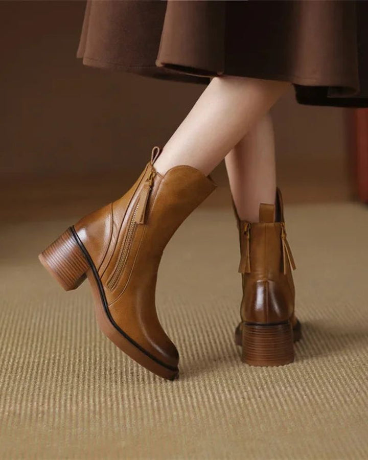 Back view of brown leather boots with zippers, styled with a dress on a beige carpet indoors.