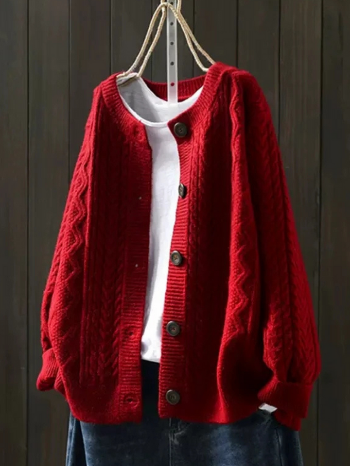 Red knitted cardigan with button closure, layered over a white shirt, hanging against a dark wood background.