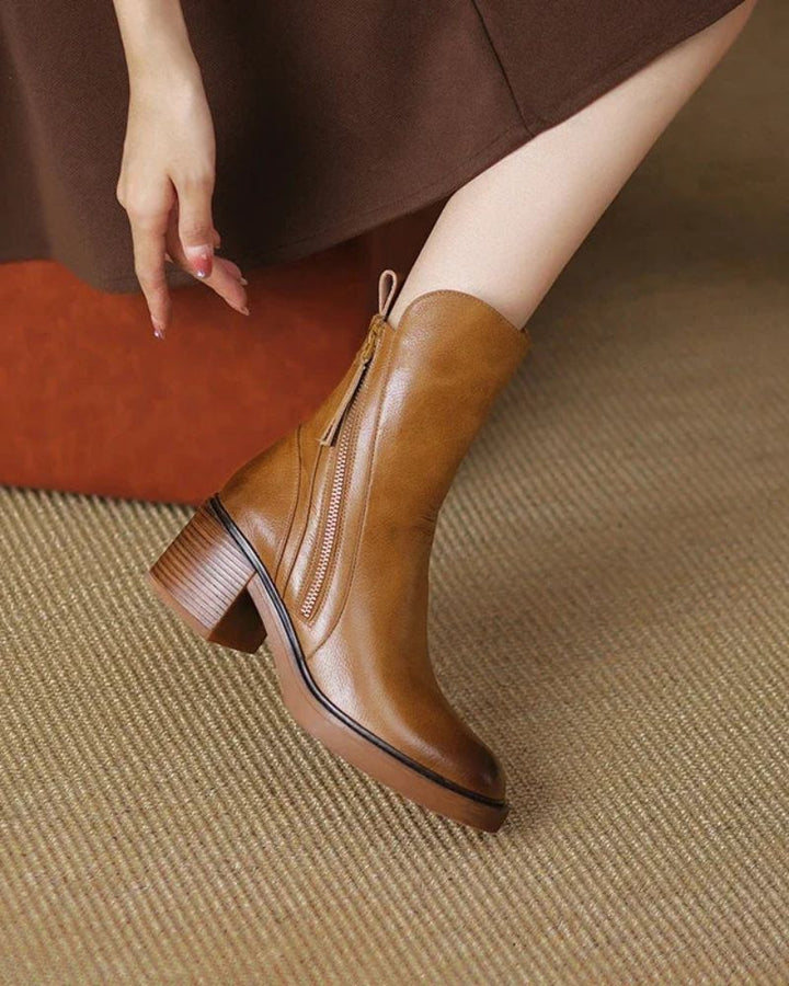 Brown leather boot with zipper, worn with a dress on a textured carpet in a warm indoor environment.