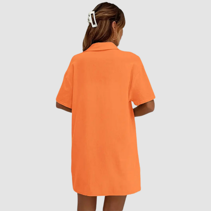Back view of woman in orange button-up dress, hair clipped, against a studio background.