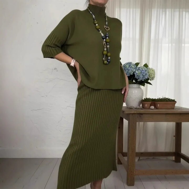 Olive green 2-piece set with ribbed skirt and loose top, accessorized with necklace in cozy room setting.