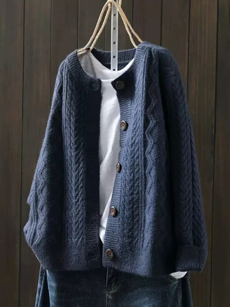 Navy knitted cardigan with button closure, layered over a white shirt, hanging against a dark wood background.