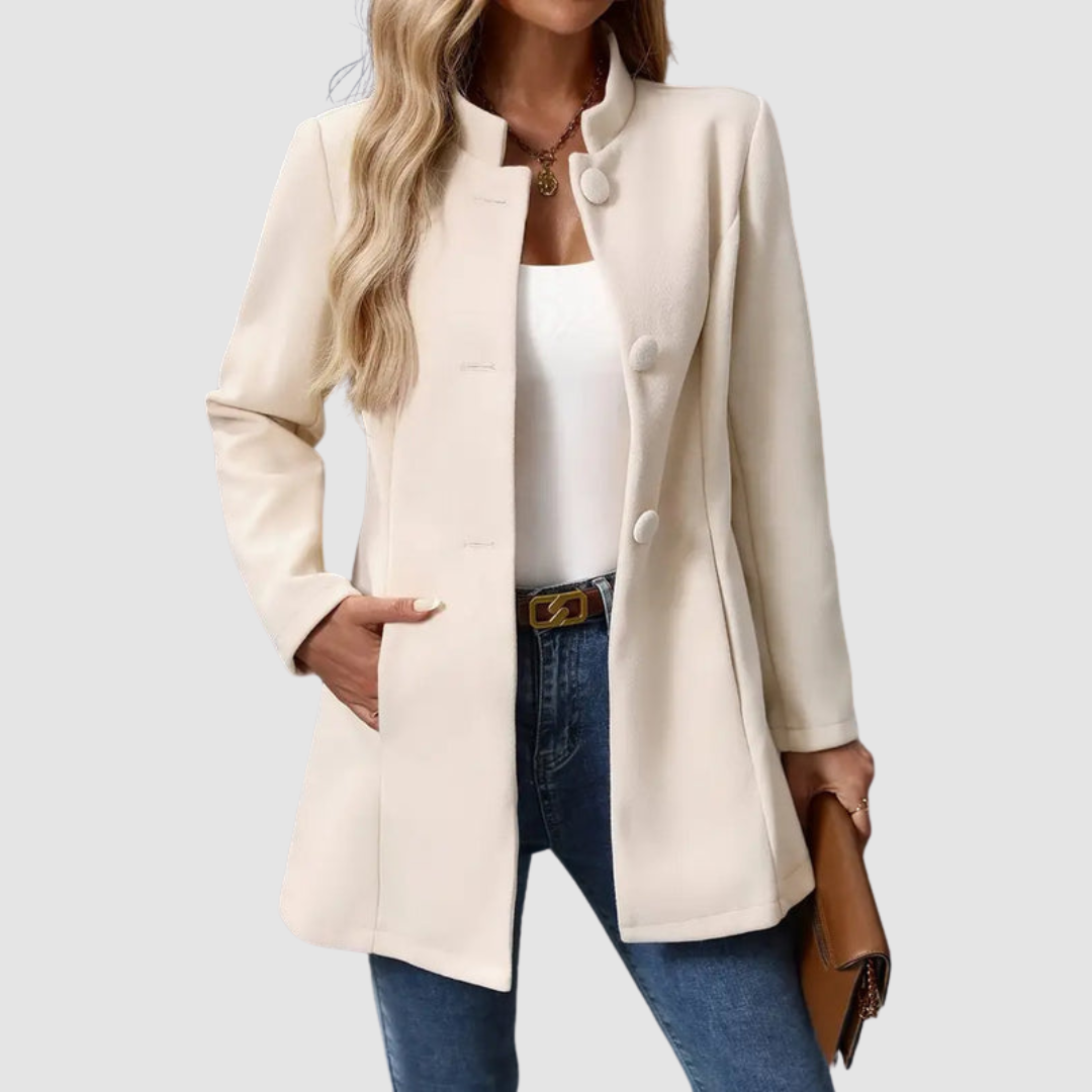 Light beige jacket with large buttons, worn over white top and jeans, holding a clutch against a plain background.
