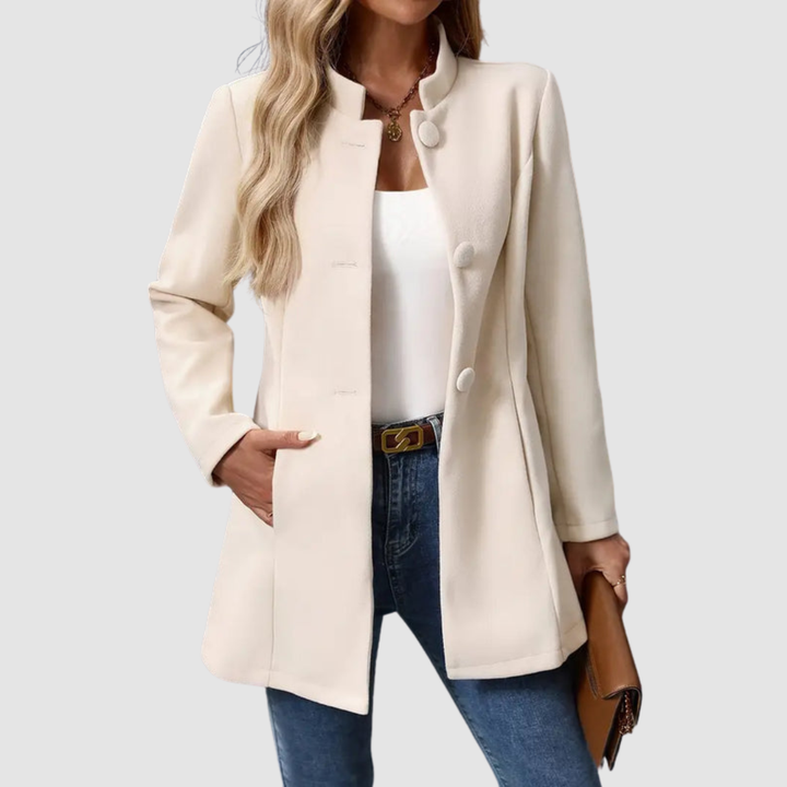 Light beige jacket with large buttons, worn over white top and jeans, holding a clutch against a plain background.